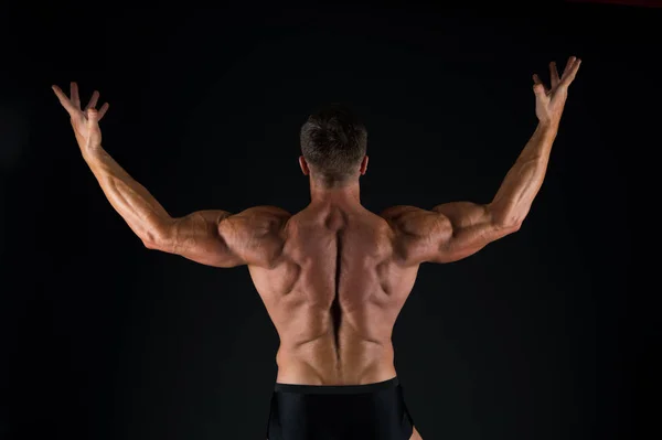 Zvyšování svalové hmoty prostřednictvím cvičení. Svalový muž pohled zpět na černé pozadí. Silný sportovec, který zvedá paže s trojhlavý a biceps. Přizpůsobit kulturista zobrazující svalovou sílu — Stock fotografie