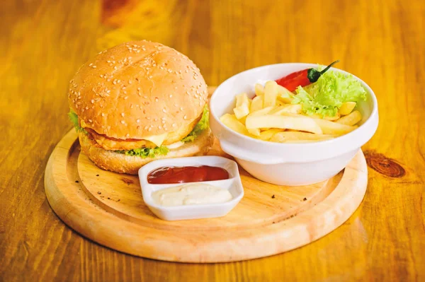 High calorie snack. Hamburger with sesame seeds and french fries and tomato sauce on wooden board. Delicious burger. Burger with cheese meat and salad. Pub food. Fast food concept. Burger menu