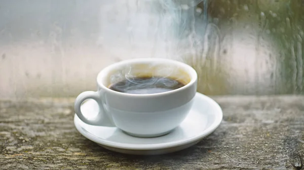 Wet glass window and cup of hot coffee. Autumn cloudy weather better with caffeine drink. Enjoying coffee on rainy day. Coffee time on rainy day. Fresh brewed coffee in white cup or mug on windowsill