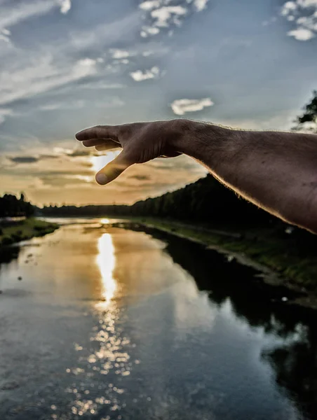 River sun reflection. Catch last sunbeam. Male hand pointing at sun in blue sky at evening time admire landscape. Capture moment to admire sunset nature beauty. Enjoy sunset above river surface — Stock Photo, Image
