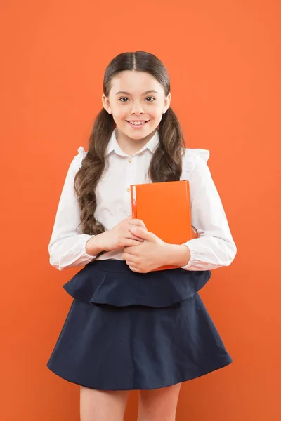 Terug naar school. Dit is mijn boek. schoolmeisje schrijft notities over oranje achtergrond. Klein meisje in schooluniform. informatieboekje. Boekenliefhebber. Gelukkig kind met oranje boek. modern schoolonderwijs — Stockfoto