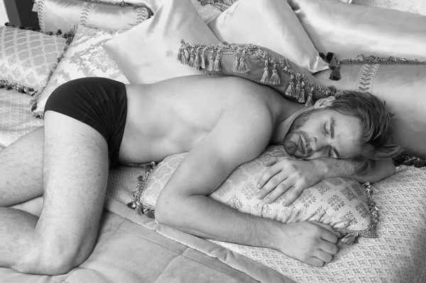 Bohemian Relax. Luxus-Apartmenthotel. Kerl entspannt sich auf dem Bett mit Vintage-Kissen im romantischen Stil. Luxus-Relax-Resort. Mann attraktiven muskulösen Körper entspannen auf King Size-Bett. Interieur aus Rokoko und Barock — Stockfoto
