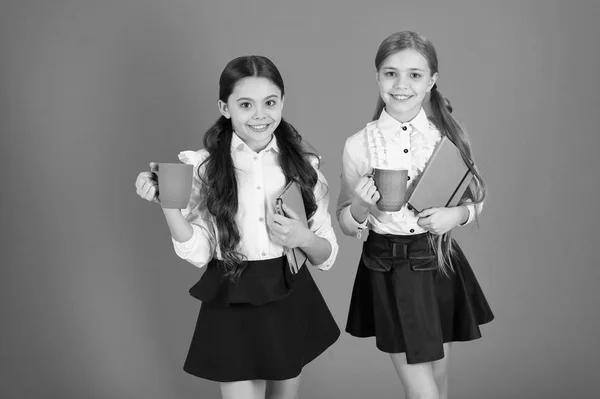 Having break relax. Drinking tea while break. School mates relaxing with drink. Enjoy being pupil. Girls kids school uniform orange background. Schoolgirl hold book or notepad and mug. School routine — Stock Photo, Image