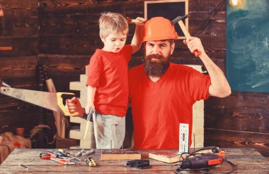 Evlat, neşeli çocuk oyuncak testere, baba ile handcrafting sırasında eğlenmek tutar. Babalık kavramı. Baba, üst koruyucu kask öğretim oğlu okul atölyesinde farklı araçları kullanmaya sakallı
