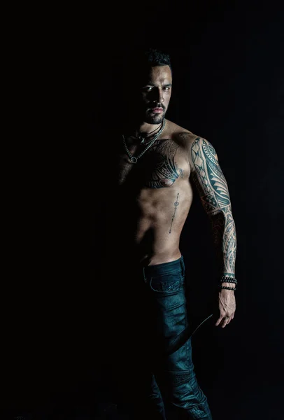 Athlete or sportsman with muscular chest and belly. Tattoo model with six pack and ab. Bearded man with tattooed body. Man with sexy bare torso in jeans. Sport or fitness and bodycare