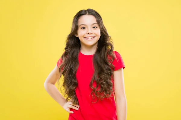 Uma menina a sorrir. menina feliz com cabelo encaracolado longo. moda e beleza. Criança hipster. felicidade infantil. salão de cabeleireiro. cuidados com a pele e cabelo natural. beleza natural. pequena beleza sorrindo — Fotografia de Stock