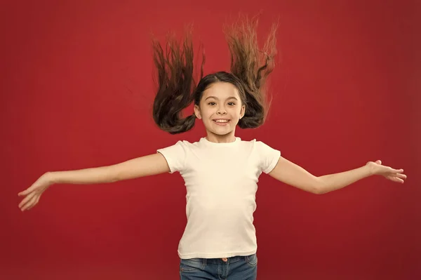 Kid smiling cute face live carefree happy life. Enjoy every moment. Young and free. Happy child girl with long hair on red background. Happiness and joy. Positive emotions. Child care and upbringing