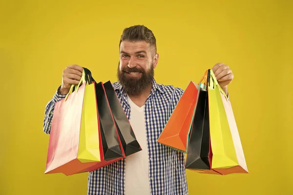 Man bearded hipster cheerful face carry paper shopping bags on yellow background. Enjoy shopping profitable deals black friday. Shopping with discount enjoy purchase. Make shopping more joyful