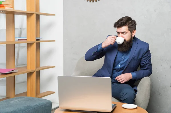 Kaffee trinken zum Frühstück. Geschäftsmann beim Kaffeetrinken am Arbeitsplatz. bärtiger Mann mit Trinkbecher am Laptop. Tee oder anderes Heißgetränk genießen — Stockfoto