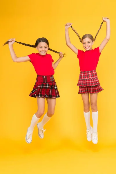 Únete a celebración. Uniforme escolar. Estilo escocés. Amigos alegres colegialas saltando fondo amarillo. Celebra la fiesta. Vacaciones escocesas. Las niñas usan vestidos a cuadros. Fiesta nacional —  Fotos de Stock