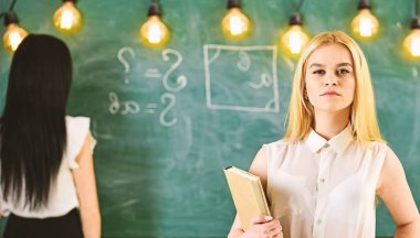 Öğrenci, formal giyim öğretmeni sınıfta durmak. Öğrenci ve kursiyer kavramı. Kız defocused kara tahta arka plan üzerinde yazma Bayan ise kendinden emin görünüyor. Çekici kadınlar için ders hazırlama