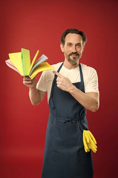 Ideal for cleaning. Eldery household worker presenting cleaning towels. Mature man pointing at cleaning cloths of assorted colors. Senior man in bib apron with rubber gloves. Household service — Stock Photo, Image