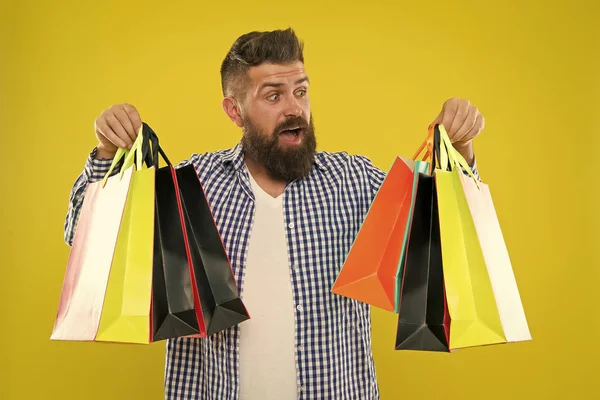 Hacer compras más alegres. Disfruta de compras rentables ofertas negro viernes. Compras con descuento disfrutar de la compra. Hombre barbudo hipster cara alegre llevar bolsas de compras de papel sobre fondo amarillo —  Fotos de Stock