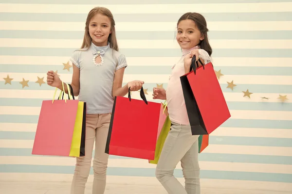 Pasando un buen rato juntos. Niños satisfechos comprando fondo rayado. Obsesionado con centros comerciales y de ropa. Concepto de descuento. Niños chicas lindas sostienen bolsas de compras. Compras temporada de descuento — Foto de Stock