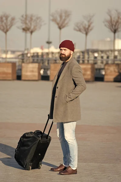 Man bearded hipster travel with big luggage bag on wheels. Let travel begin. Traveler with suitcase waiting transportation to airport railway station. Ready to travel. Carry travel bag. Business trip