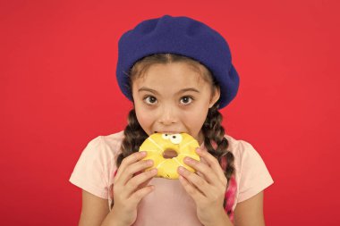 Kız tatlı çörek elinde kırmızı camlı arka plan tutun. Çocuk oynak kız donut yemeye hazır. Şeker dükkanı ve ekmek kavramı. Pişmiş Donuts büyük fanlar çocuklar. Resist taze yapılmış çörek imkansız