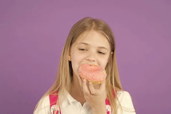 A criança come donut no fundo violeta. Menina mordida rosquinha de anel envidraçado. Conceito de loja de doces. Infância e felicidade. Um miúdo com comida de plástico. Que bom humor. Alimentação insalubre e lanche — Fotografia de Stock