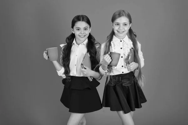 Consumo de desayuno. Niños de la escuela desayunando por la mañana. Chicas pequeñas disfrutando de su desayuno escolar. Colegialas lindas sosteniendo tazas y libros. Niños pequeños que beben té matutino o leche —  Fotos de Stock