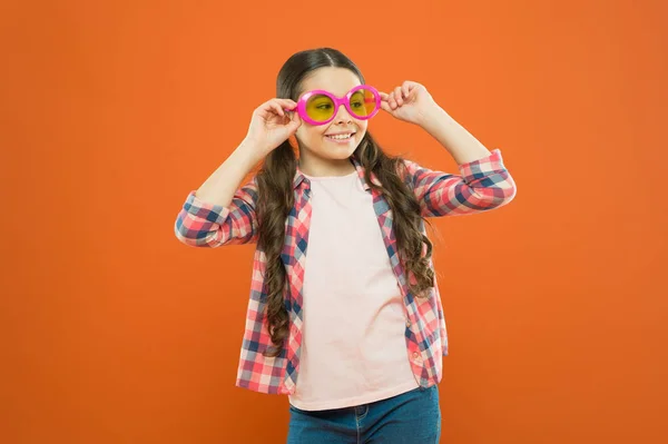 Модні сонцезахисні окуляри підтримують захист очей дітей і добре виглядають. Невелика модель моди на помаранчевому фоні. Чарівна маленька дівчинка в модному аксесуарі. Мила дитина з модним виглядом — стокове фото