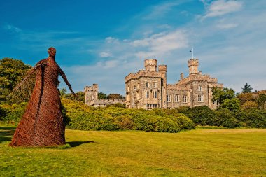 Wicker woman statue and castle in Stornoway, United Kingdom. Willow sculpture on green grounds of Lews Castle estate. Architecture and design. Landmark and attraction. Summer vacation and wanderlust clipart