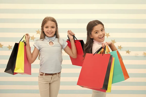 Bambini soddisfatti shopping sfondo a strisce. Ossessionato da centri commerciali e abbigliamento. Concetto sconto. Bambini ragazze carine tengono borse della spesa. Shopping stagione di sconto. Trascorrere un grande momento insieme — Foto Stock