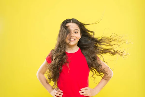 Essere naturali è più elegante. Adorabile bambina sorridente su sfondo giallo. Ragazza bruna con lunghi capelli ondulati in stile moda. Carina la ragazzina di moda. Ragazza piccola con sguardo di bellezza felice — Foto Stock