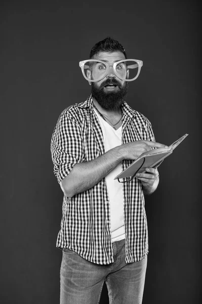 Φρικιό και geek. Γενειοφόρος άνδρας στο κόμμα γυαλιά ανάγνωσης βιβλίου. Μελέτη nerd κρατώντας το βιβλίο του μαθήματος. Αρσενικό φοιτητής πανεπιστημίου με σημειώσεις. Σπασίκλα βιβλίο φορώντας φανταχτερά γυαλιά — Φωτογραφία Αρχείου