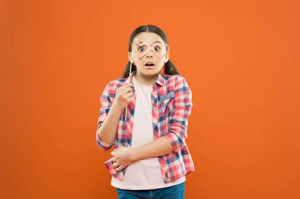 I am surprised at you. Surprised small child looking through prop party glasses on orange background. Little girl keeping mouth opened wide on cute surprised face. Being pleasantly surprised