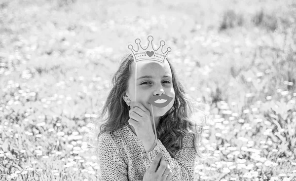 Concepto de reina del humor. Chica se sienta en la hierba en Grassplot, fondo verde. Chica en la cara alegre pasar el ocio al aire libre. Niño posando con labios sonrientes de cartón y corona para sesión de fotos en el prado —  Fotos de Stock