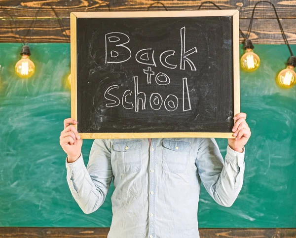 Concept de début d'année scolaire. Enseignant sans visage tient tableau noir avec titre de retour à l'école. L'homme accueille les étudiants, tableau sur fond. L'enseignant tient un tableau devant le visage — Photo