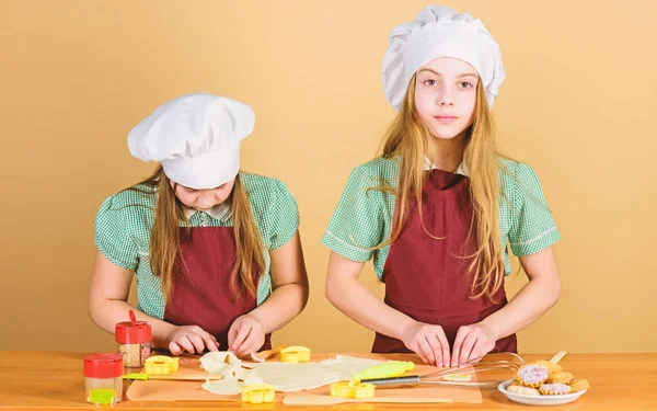 楽しいジンジャー生地を持つ女の子姉妹。自家製クッキー最高。子供たちは一緒にクッキーを焼く。キッズエプロンとシェフの帽子料理。家族のレシピ。料理教育。母の日。ベーキングジンジャークッキー — ストック写真