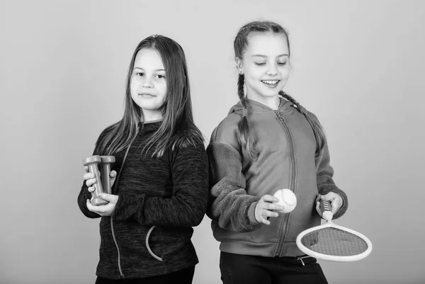 私たちはスポーツが大好きです。子供は全く異なるスポーツに優れるかもしれません。友人は訓練の準備ができています。子供たちが楽しむスポーツを見つけるのを助ける方法。スポーツ用品ダンベルとテニスラケットを持つ女の子かわいい子供たち — ストック写真