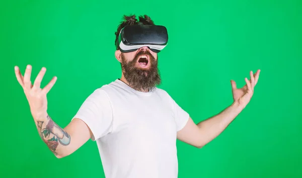 Muž s vousy ve VR brýlích, zelené pozadí. Pojem energie. Hipster na křičící tvář zvedá ruce při interakci ve virtuální realitě. Chlápek s displejem namontovaným na hlavě interaguje ve VR — Stock fotografie