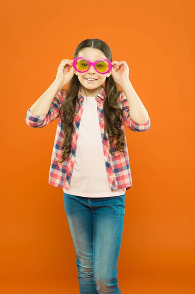 Está na moda. Menina de festa na moda no fundo laranja. Adorável festa menina vestindo óculos extravagantes. Criança pequena bonito olhando através de óculos de festa com filtro de cor. Preparação para uma festa legal — Fotografia de Stock