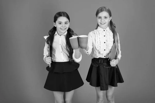 Té para dos y dos para el té. Niños pequeños que beben té de la mañana o leche. Colegialas lindas sosteniendo tazas y libros. Chicas pequeñas disfrutando el desayuno escolar. Niños en edad escolar desayunando por la mañana — Foto de Stock