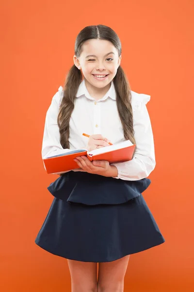 Estudante escrevendo notas sobre fundo laranja. menina pequena em uniforme escolar. estudante segurando livro lição. obter informações livro de formulário. de volta à escola. menina bonito segurar bloco de notas ou diário. Diário para menina — Fotografia de Stock