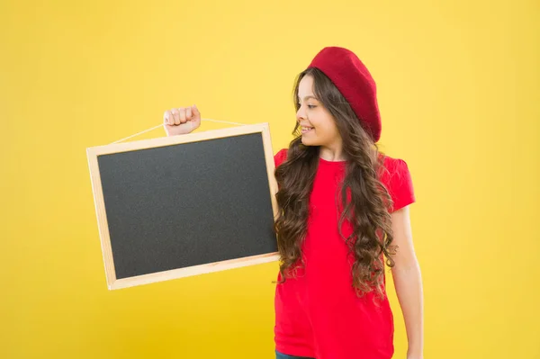 Chica de la escuela feliz en boina parisina. Niña pequeña con tablero, espacio para copiar. tablero para la publicidad del anuncio. de vuelta a la escuela. Compras escolares. Moda infantil. Mejor servicio — Foto de Stock