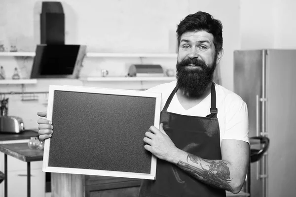 Experimenta esta refeição. Cozinhe anunciando seu produto. Restaurante ou menu de café. Anúncio. Homem maduro. Cozinheiro barbudo. Hipster na cozinha. Homem barbudo de avental vermelho. Homem chef com bordo, espaço de cópia — Fotografia de Stock