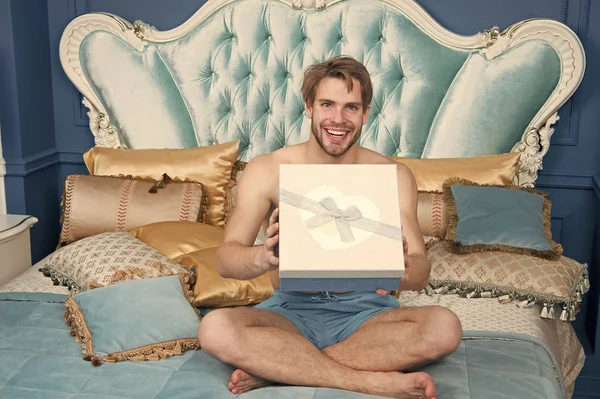 Already found his birthday gift in bed. Happy man holding birthday present wrapped in box. Sexy man smiling with birthday gift. Handsome guy with box on birthday morning. Happy birthday to you