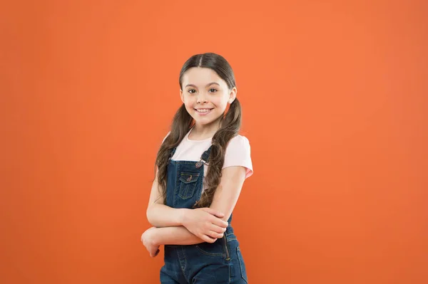毎日素晴らしいこと。ファッションの女の子。オレンジの背景にかわいい小さなファッションモデル。ファッションルックを持つ小さな子供。カジュアルなファッションスタイルで長いブルネットの髪を持つ愛らしい子供 — ストック写真