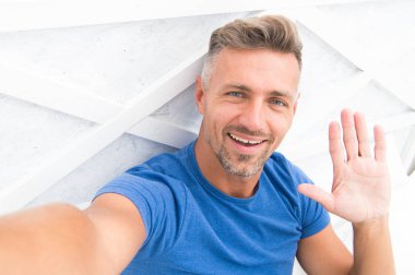Merhabalar. Adam fotoğraf çeken akıllı telefondan el sallıyor. Çevrimiçi video yayınlanıyor. Gezici internet. Blog için çekim. Olgun bir blogcu. İnternet günlüğü içeriği. Kişisel blog konsepti. Günaydın.