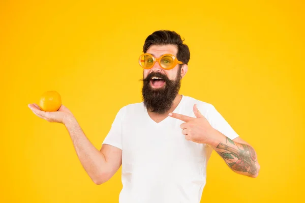Хіпстер з бородою в літньому настрої. Веселий хлопець тримає стиглі апельсинові цитрусові. Літня відпустка. Чоловік бородатий хіпстер в помаранчевих сонцезахисних окулярах на жовтому тлі. Джерело оновлення. Літнє харчування — стокове фото