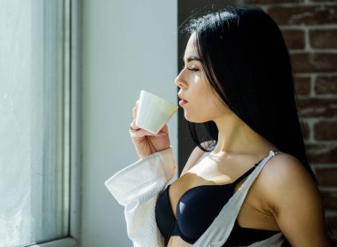 Kız seksi göğüsler pencere kenarında kahve içme. Çekici kadın iç çamaşırı evde rahatlatıcı. Mükemmel kahve zamanı. Ama önce kahve. Huzur ve huzur. Kremsi kapuçino yudumlayın. Sabah ritüeli