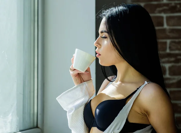 Chica senos sexy beber café cerca de alféizar de la ventana. Ropa interior femenina atractiva relajante en casa. Hora del café perfecta. Pero primero café. Tranquilidad y paz. Un sorbo de capuchino cremoso. Ritual matutino — Foto de Stock