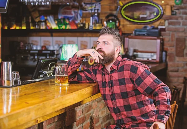 Order alcohol drink. Bar is relaxing place have drink and relax. Man with beard spend leisure in dark bar. Brutal hipster bearded man sit at bar counter drink beer. Hipster relaxing at bar with beer