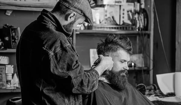 Concetto di stile di vita hipster. Un cliente hipster che si taglia i capelli. Il barbiere con tagliacapelli lavora sull'acconciatura per lo sfondo del barbiere. Barbiere con taglio di capelli clipper sul tempio del cliente — Foto Stock