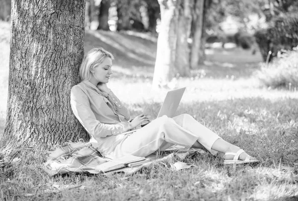Arbeta utomhus fördelar. Kvinna med laptop datorarbete utomhus lean på trädstam. Utbildning teknik och internet koncept. Flicka arbete med laptop i park sitta på gräset. Naturliga miljön office — Stockfoto