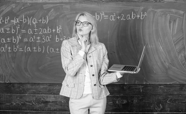 Woman wear eyeglasses holds laptop surfing internet. Educator smart clever lady with modern laptop searching information chalkboard background. Online schooling concept. Educational site for teachers Stock Image