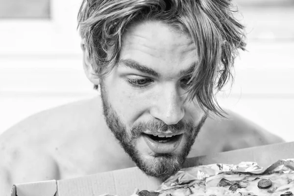 Sexy man eat pizza lying on bed. Student is at home on the bed in a bright apartment eating a tasty pizza. Man bearded handsome bachelor eating cheesy food for breakfast in bed. People like pizza.