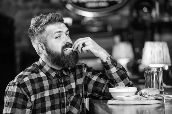 Man with beard drink beer eat burger menu. Enjoy meal in pub. Brutal hipster bearded man sit at bar counter. High calorie snack. Hipster relaxing at pub. Pub is relaxing place to have drink and relax